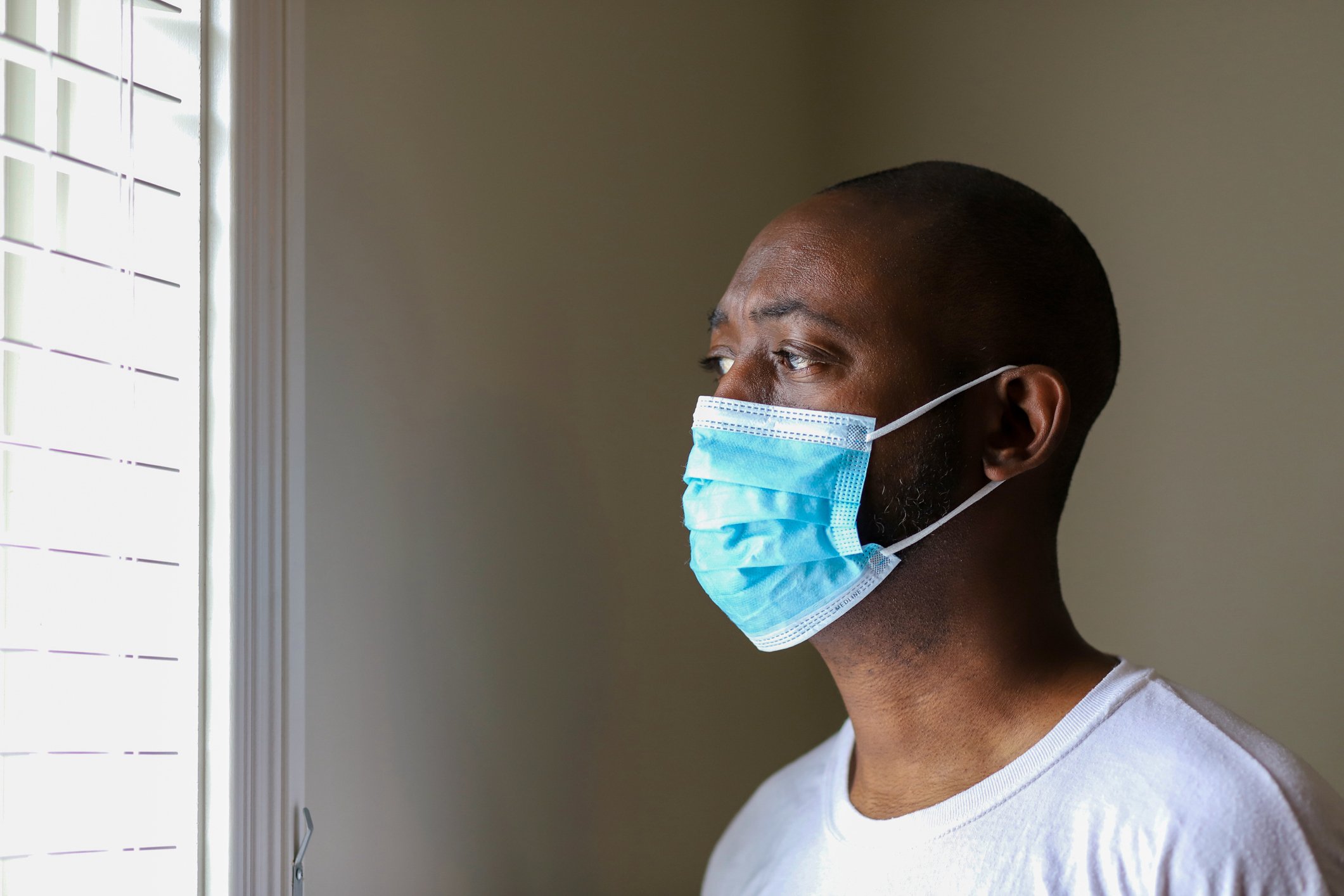 man with face mask in house looking out window